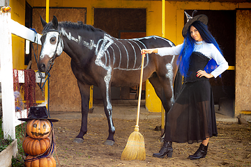 Image showing A witch on a farm stands next to a horse and an evil pumpkin man