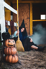 Image showing A girl dressed as a witch with a broom squatted by the fence at the Halloween celebration