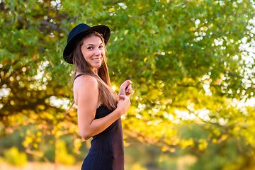 Image showing Portrait of a beautiful girl, turned and looked into the frame, against a background of blurred foliage