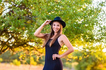 Image showing Portrait of a beautiful girl on a background of blurry foliage, the girl holds a hat with one hand