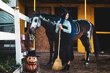 Image showing A girl dressed as a witch stands by a corral on a farm next to a horse