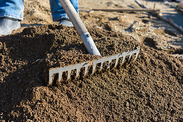 Image showing The gardener loosens the ground with a rake