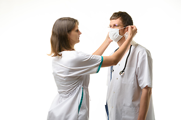 Image showing The nurse puts a medical mask on the doctor\'s face with glasses