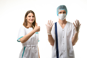 Image showing A nurse stands next to a doctor in a medical mask, a cap and sterile gloves and happily points up