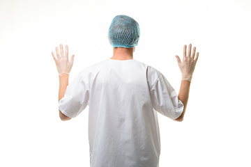 Image showing A male doctor stands with his hands raised up, gloves are on, a mask and a hat are on his head, rear view