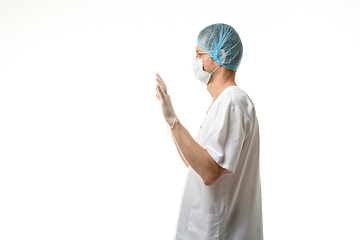 Image showing A male doctor stands with his hands raised up, gloves are on, a mask and a hat are on his head, side view