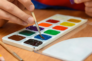 Image showing The child\'s hands are dipping with a brush in the desired color of watercolor paints