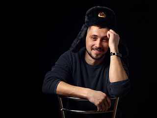 Image showing Portrait of a smiling man of thirty years of Caucasian appearance in a Soviet officer\'s fur hat on a black background