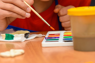 Image showing A girl dips a brush in paint of the desired color while painting a craft from salt dough, close-up