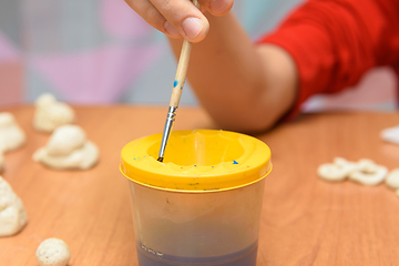 Image showing A girl dips a brush into a glass of water painting figures from salt dough