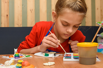 Image showing A girl dips a brush in paint of the desired color while painting a craft from salt dough