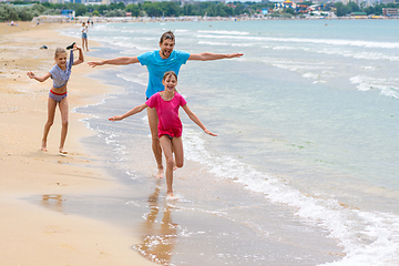 Image showing Dad with two children running merrily along the seashore