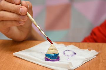 Image showing A girl paints a pyramid of salt dough with different colors, close-up