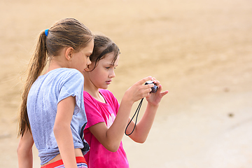 Image showing Two girls look at photos on the screen of a digital camera while on the sea sandy beach