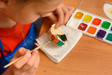Image showing A girl paints a craft from salt dough with watercolors, top view