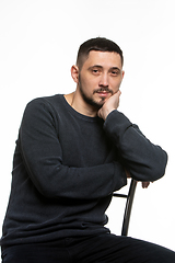 Image showing Portrait of an ordinary man in a dark plain sweater sitting on a high-backed chair