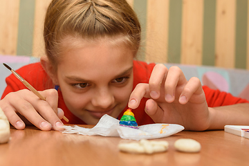 Image showing A girl bending over looks at a painted figurine made of salt dough