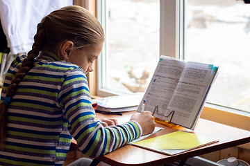 Image showing Schoolgirl sits at the table by the window and does homework