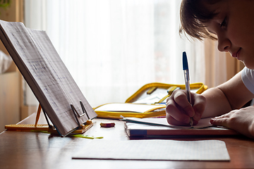 Image showing Girl doing homework sitting at the table by the window