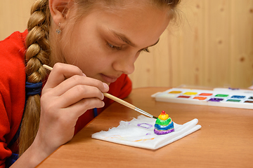 Image showing A girl carefully paints a figurine made of salt dough