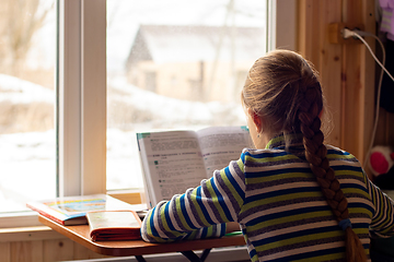 Image showing Back view of a schoolgirl sitting by the window and doing homework