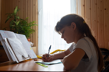 Image showing Girl does homework while sitting at the table in the room of a country house