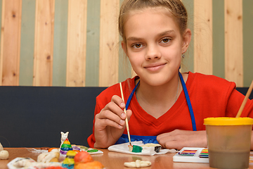 Image showing A girl paints a craft from salt dough with watercolors and looked into the frame