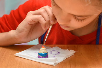 Image showing A girl carefully paints a figurine made of salt dough, close-up