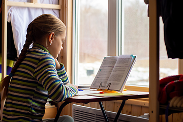 Image showing Schoolgirl carefully reads the task in the textbook while doing homework while sitting by the window