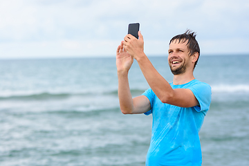 Image showing A man communicates via video communication using a mobile phone while relaxing on the sea