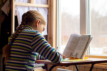 Image showing Girl doing homework sitting at the table by the window