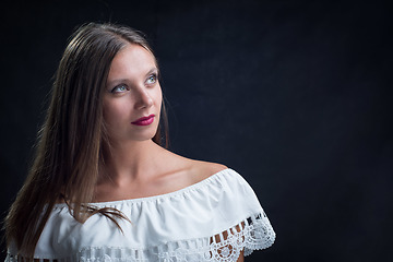 Image showing Portrait of a beautiful girl looking up in a loose white dress on a black background