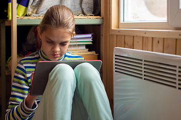 Image showing The girl plays in the tablet, sitting in a secluded corner next to the battery