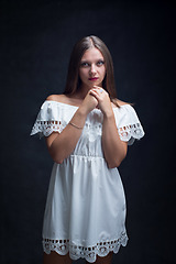 Image showing Portrait of a beautiful girl in a loose white dress on a black background