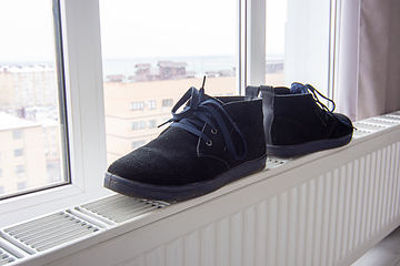 Image showing Suede winter boots are dried on a radiator near the window