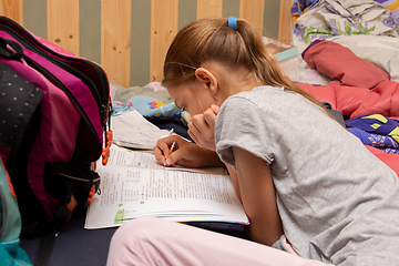 Image showing Schoolgirl does her homework on a spread out couch piled high with things