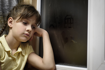 Image showing A frustrated girl sits at a foggy window and is sad