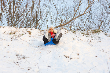 Image showing A girl is rolling down a snow-covered slide while sitting on a plastic ice floe