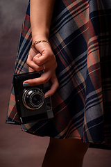 Image showing Girl\'s hand holding a camera near the hem of the dress, vertical frame, studio photography on a gray background