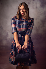 Image showing Portrait of a beautiful girl on a gray background, the girl holds a black handbag with two hands in front of her