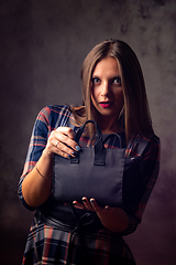 Image showing A beautiful girl holds a handbag in front of her and looked into the frame with big eyes