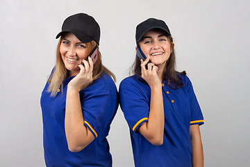 Image showing Mother and daughter are standing with their backs to each other, talking on the phone and looking into the frame