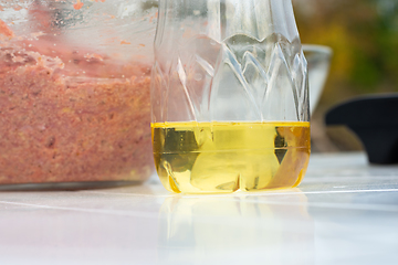 Image showing On the table is sunflower oil in a plastic bottle, in the background is a glass bowl with minced meat for cutlets