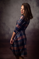 Image showing Portrait of a beautiful girl in a checkered dress, the girl is turned sideways