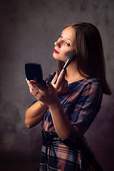 Image showing Girl powders her face with a brush looking in the mirror, studio photo on a gray background