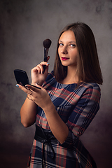 Image showing The girl powders her face with a brush while looking in the mirror, the girl was distracted and looked into the frame, studio photography on a gray background