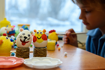 Image showing In the foreground there are decorated children\'s Easter eggs, in the background a child is painting an egg