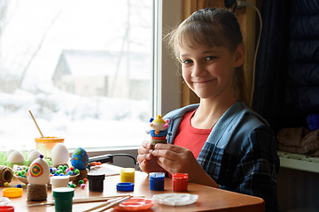 Image showing The girl happily looks into the frame while holding a decorated chicken egg craft in her hands