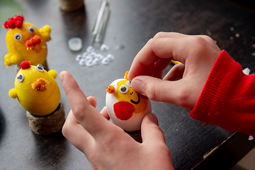 Image showing A girl decorates an egg for the Easter holiday by carefully gluing funny eyes to it