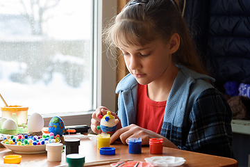 Image showing A girl sitting by the window sticks decorative elements on Easter eggs